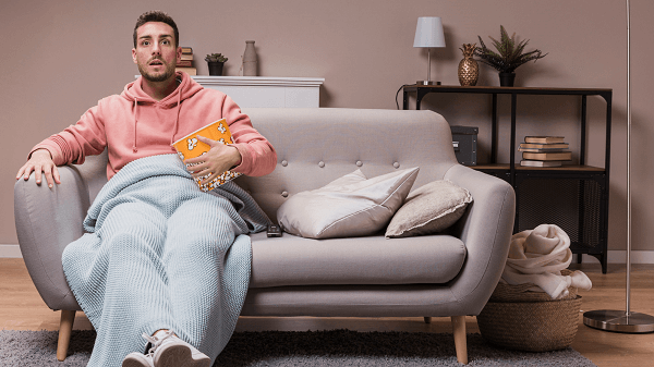 5 Programas de TV que roubam seu dinheiro - homem sentado no sofá come pipoca e assiste tv