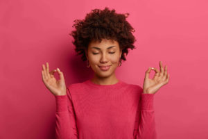 mulher negra com roupa rosa, fazendo sinal de meditação