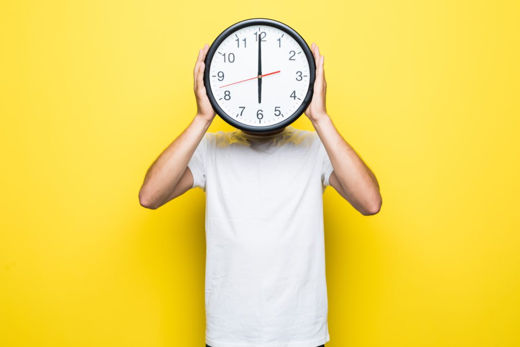 Homem com relógio no rosto, mostrando que está na hora de deixar de procrastinar