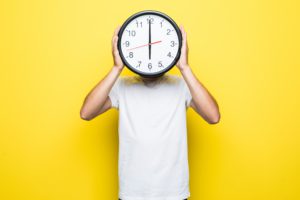 Homem com relógio no rosto, mostrando que está na hora de deixar de procrastinar