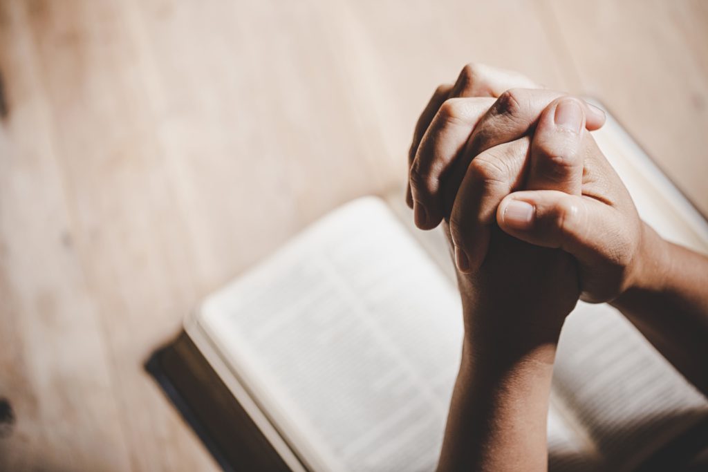 Mãos unidas em posição de oração sobre livro - espiritualidade